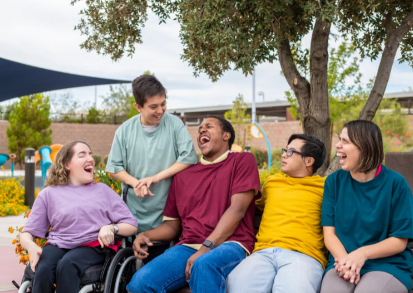 A diverse group of young people including NDIS participants laughing together at an outdoor community participation event with Noon Care