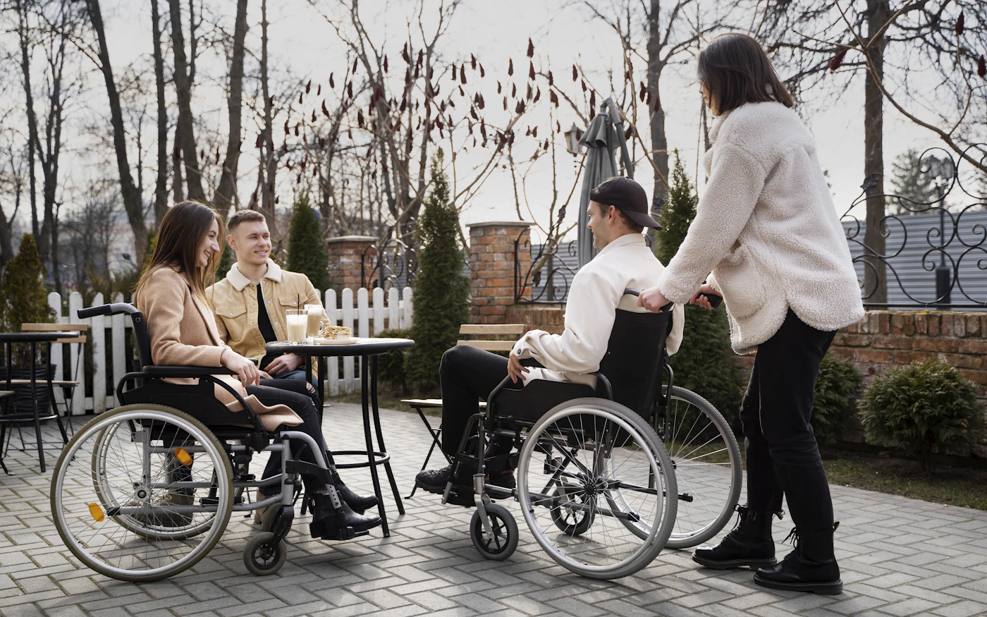 A group of friends, two using wheelchairs, sharing drinks at an outdoor cafe, representing real-world community participation